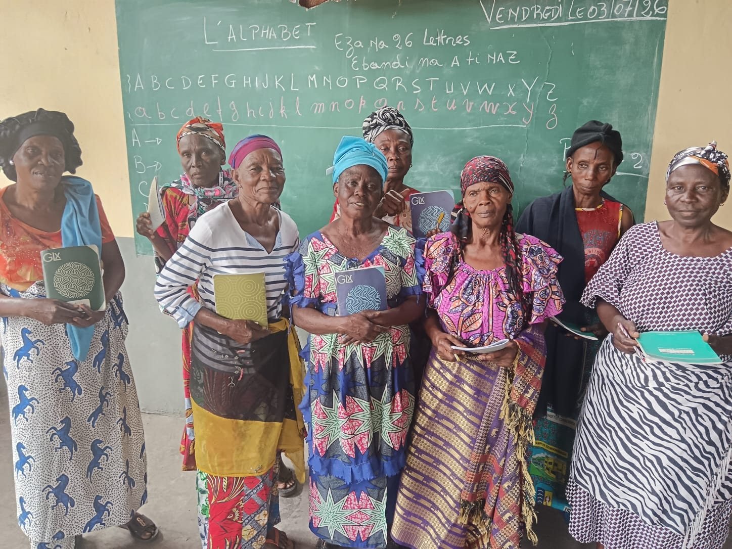 Des veuves du cours d'alphabétisation, cahiers en main, devant le tableau à Kinshasa